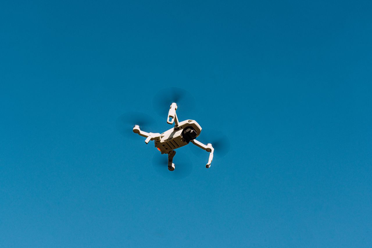 Services A drone flying against a clear blue sky, capturing aerial views.