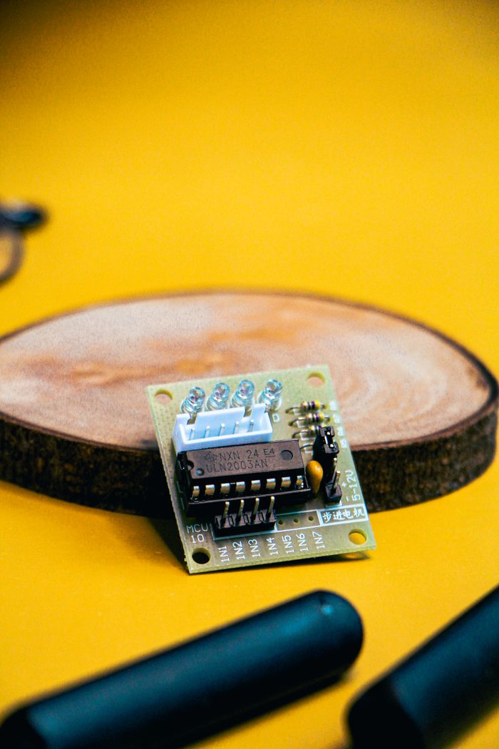 Close-up of a small electronic circuit board on a wooden disc with a yellow background.